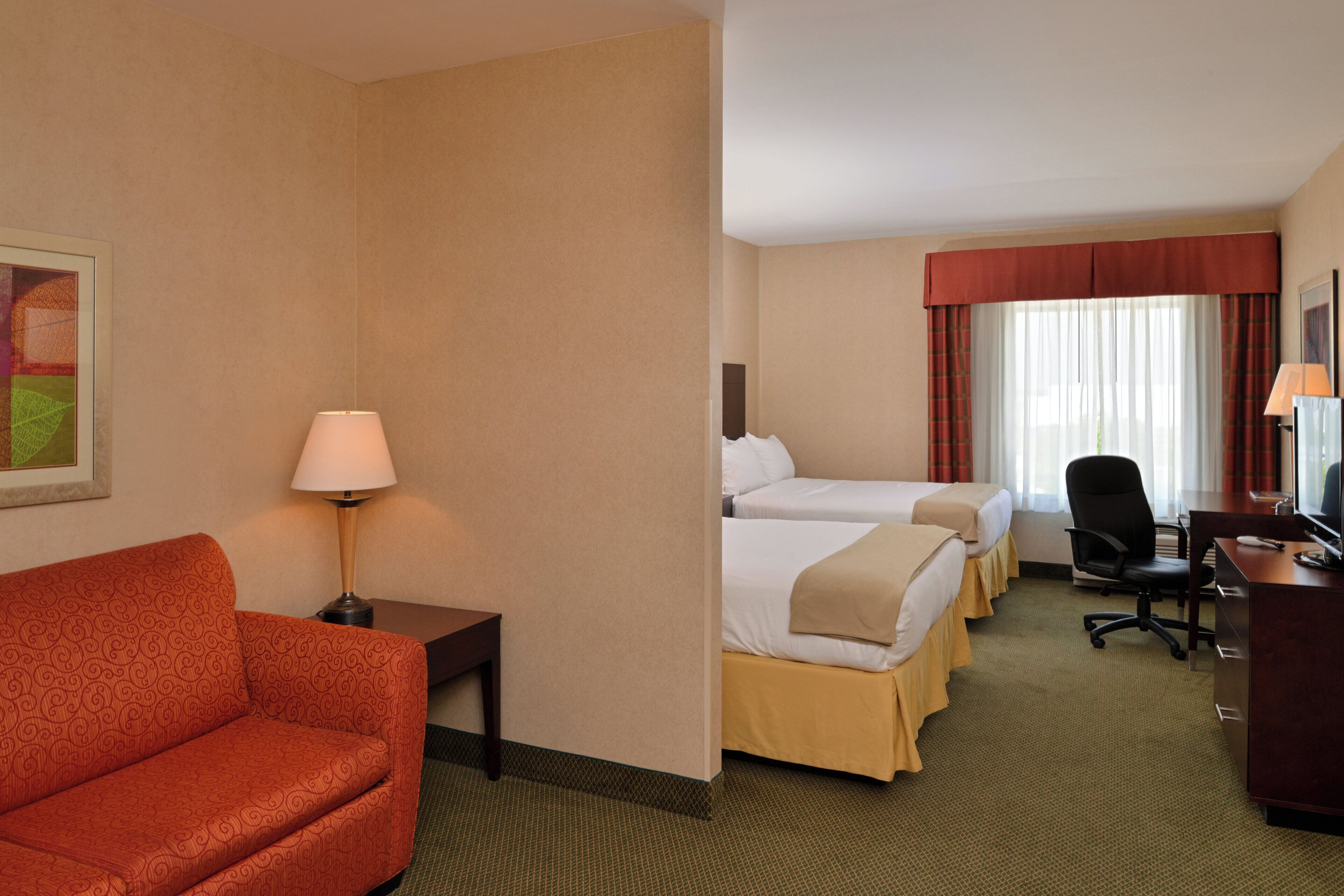 Una habitación de hotel con un sofá, dos camas, un escritorio, una silla y una lámpara.
