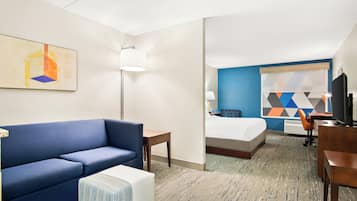 A hotel room with a blue sofa, a bed, a desk, and a TV.