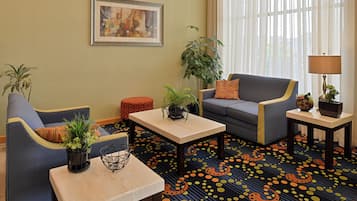 Een hotelkamer met een bank, fauteuil, bijzettafeltje en een potplant.