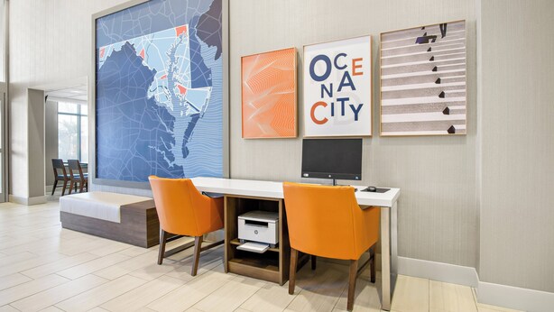 A modern office space with a large map, framed artwork, and a desk with two orange chairs. - Holiday Inn Express Hotel & Suites Ocean City by IHG (Ocean City)