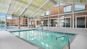 Una piscina interior con señalización clara, techo cubierto y vista a un edificio de ladrillo.