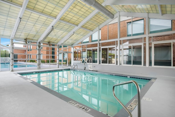 An indoor swimming pool with clear markings, a covered roof, and a view of a brick building outside.