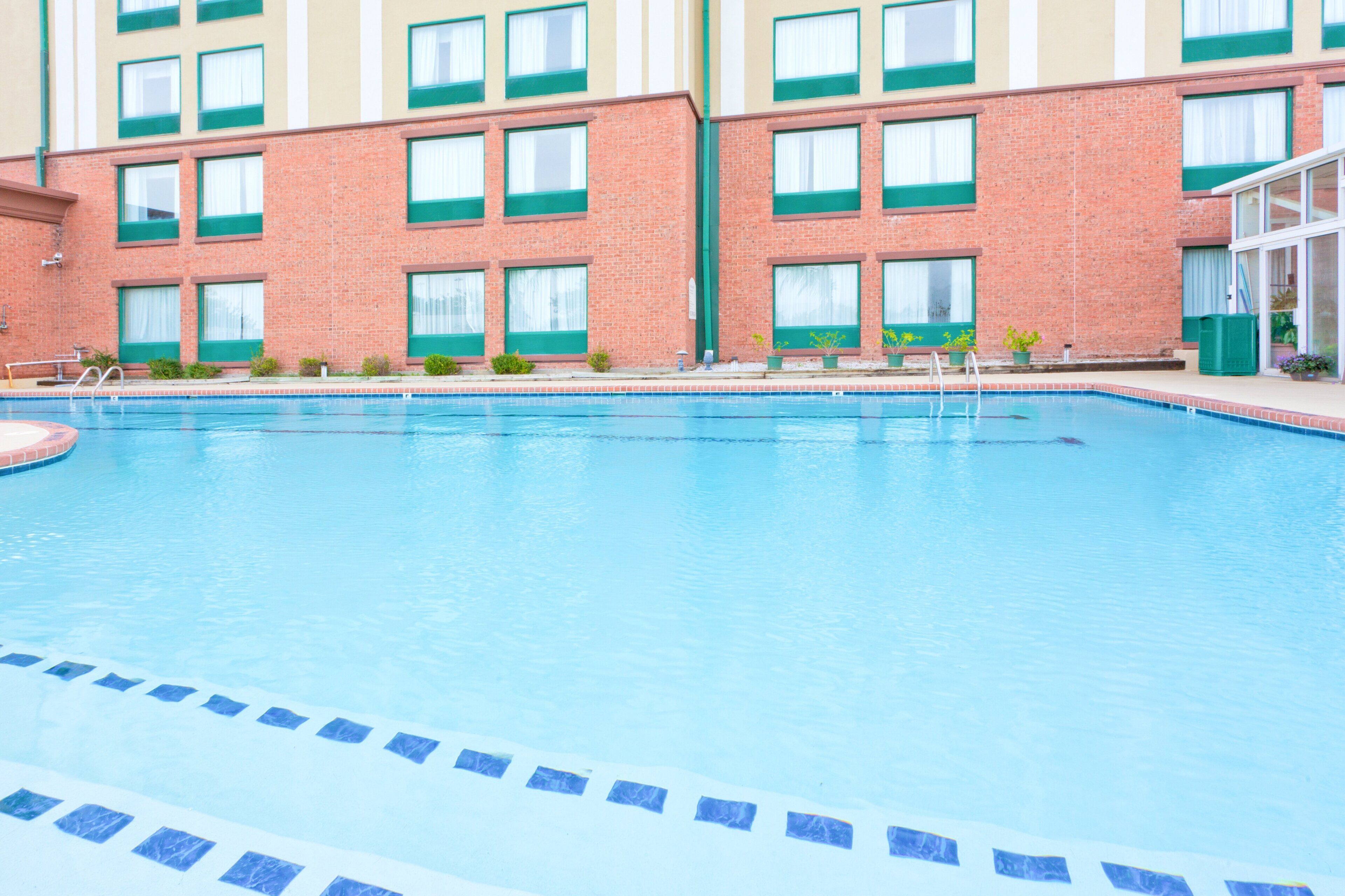 A swimming pool with a tiled edge, surrounded by a brick building with multiple windows and a door.