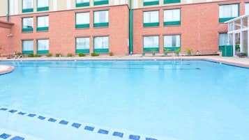 A swimming pool with a tiled edge, surrounded by a brick building with multiple windows and a door.