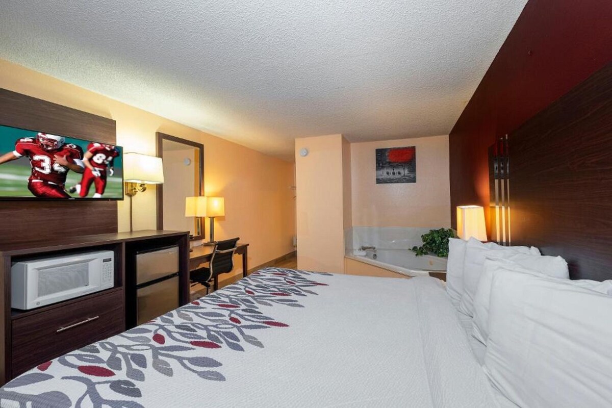 Una habitación de hotel con una cama, un escritorio con lámpara, un televisor y un cuadro en la pared.