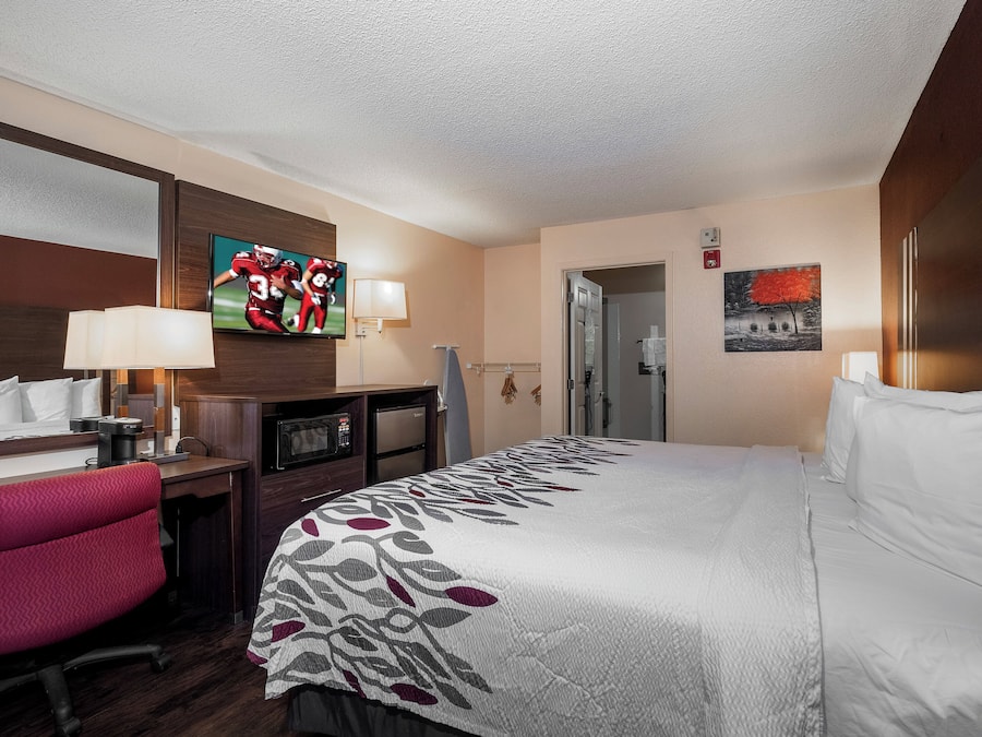 A hotel room with a bed, a desk with a chair, a television, and a painting on the wall.