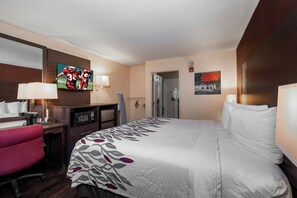 Ein Hotelzimmer mit Bett, Schreibtisch mit Stuhl, Fernseher und einem Bild an der Wand.