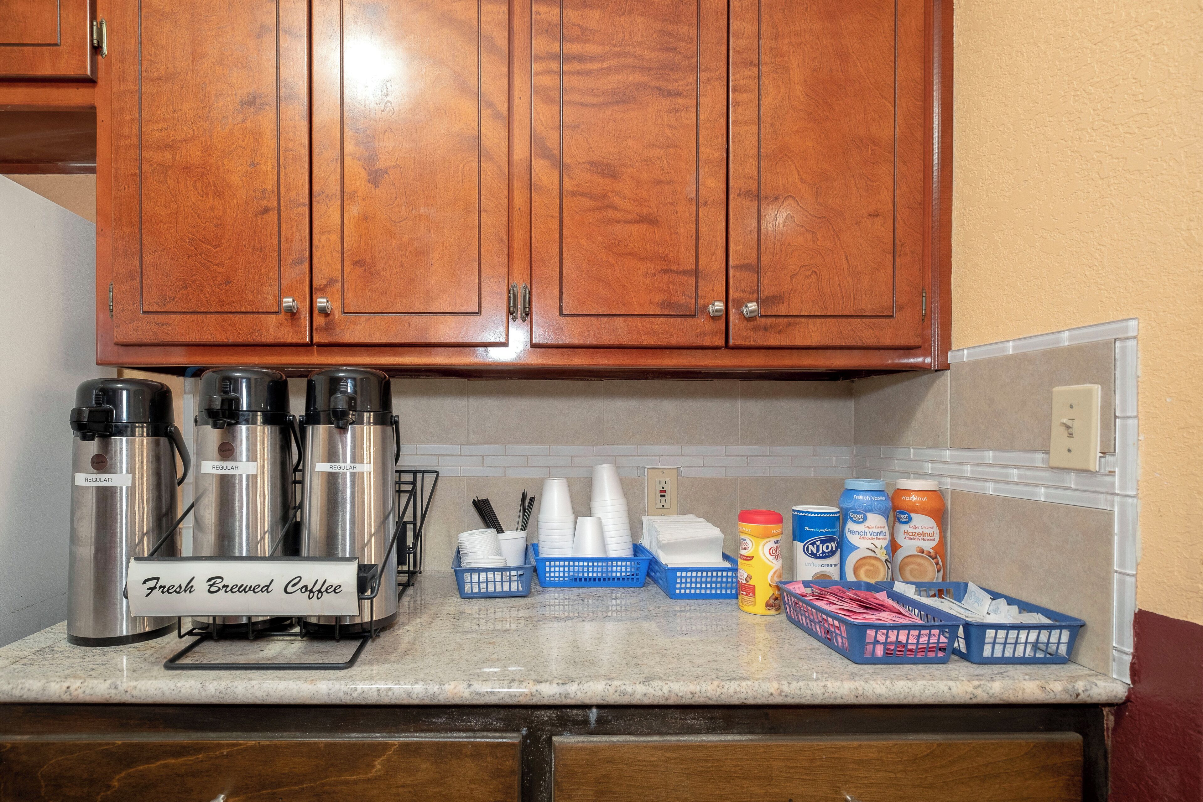 A kitchen with wooden cabinets, a coffee station with thermos cups, and various kitchen supplies.
