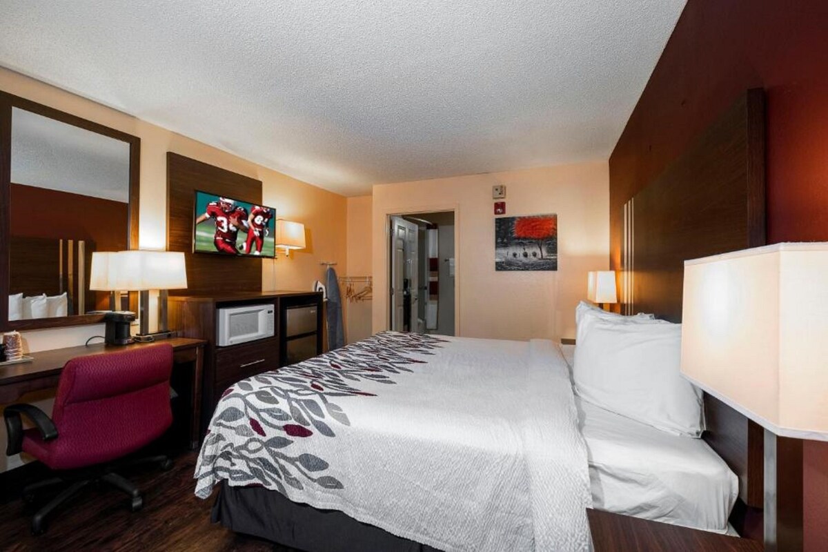 Habitación de hotel con cama, escritorio, silla, televisor y obras de arte en las paredes.