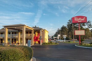 Un hotel Red Roof Inn con una zona de estacionamiento techada y una escalera roja que conduce a la entrada.