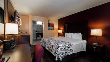 A hotel room with a bed, bedside lamps, a desk with a coffee maker, a chair, and a painting on the wall.
