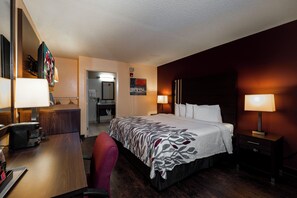 A hotel room with a bed, bedside lamps, a desk with a coffee maker, a chair, and a painting on the wall.