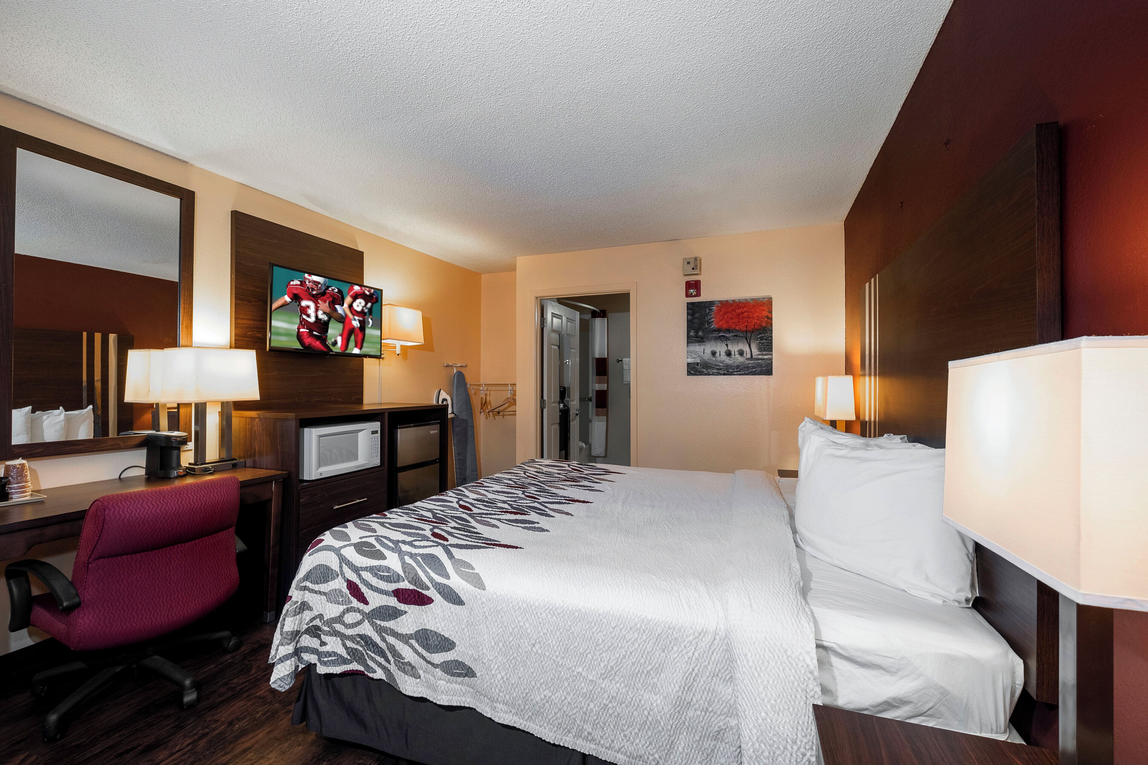 A hotel room with a bed, desk, chair, television, and a painting on the wall.