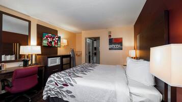 A hotel room with a bed, desk, chair, television, and a painting on the wall.