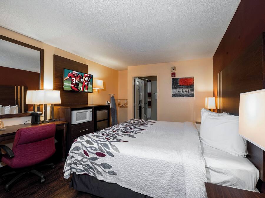 A hotel room with a bed, desk, chair, television, and a painting on the wall.