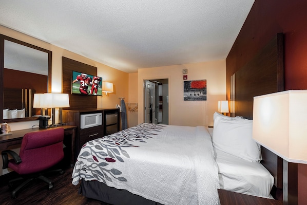 Una habitación de hotel con cama, escritorio, silla, televisión y un cuadro en la pared.