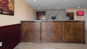 Zona de recepción de un hotel con un mostrador de madera, un cuadro de flores en la pared, un letrero de Red Roof Inn, una pantalla digital que anuncia Wi-Fi gratuito y una pared de piedra.