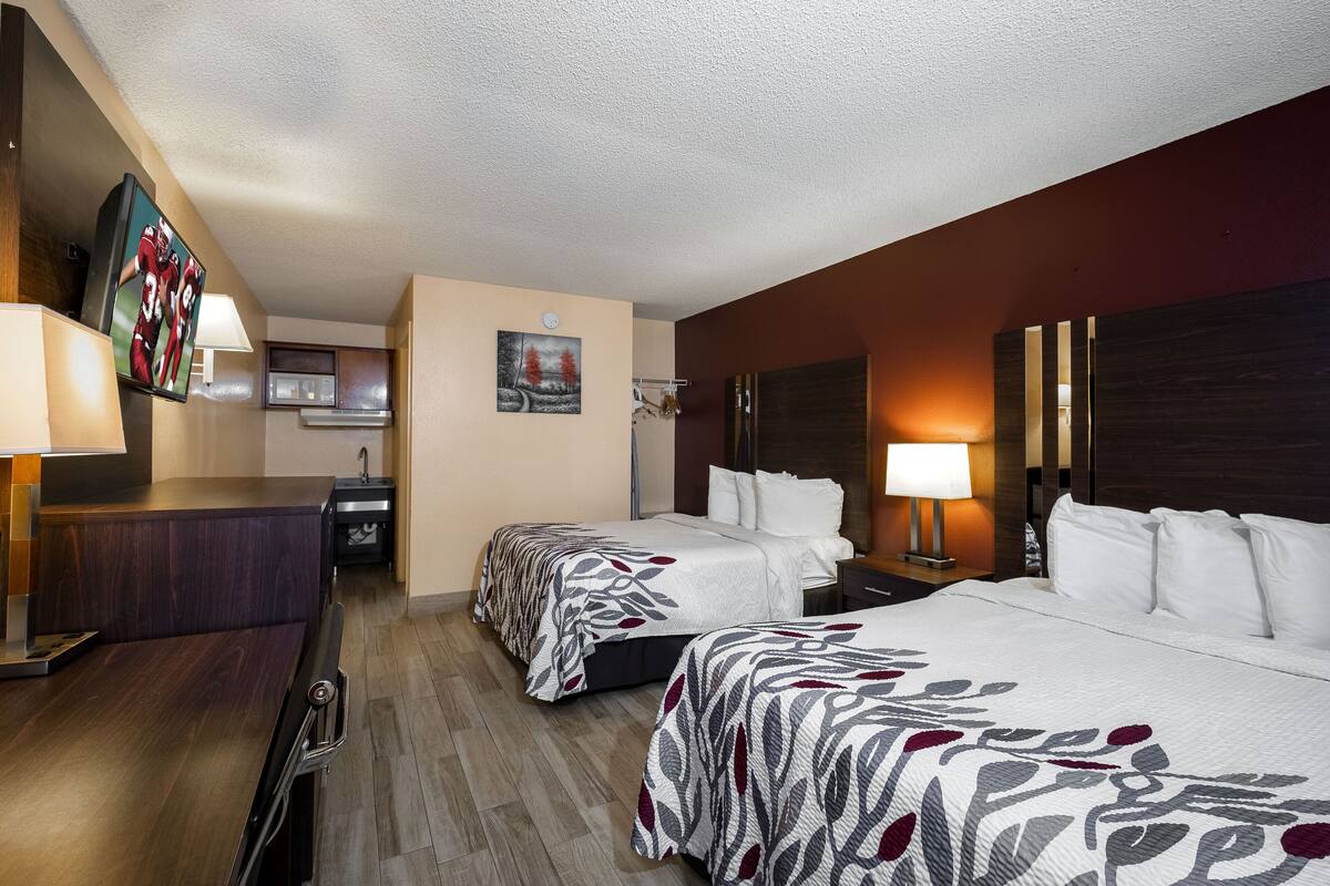A hotel room with two beds, a desk, a TV, and a painting on the wall.