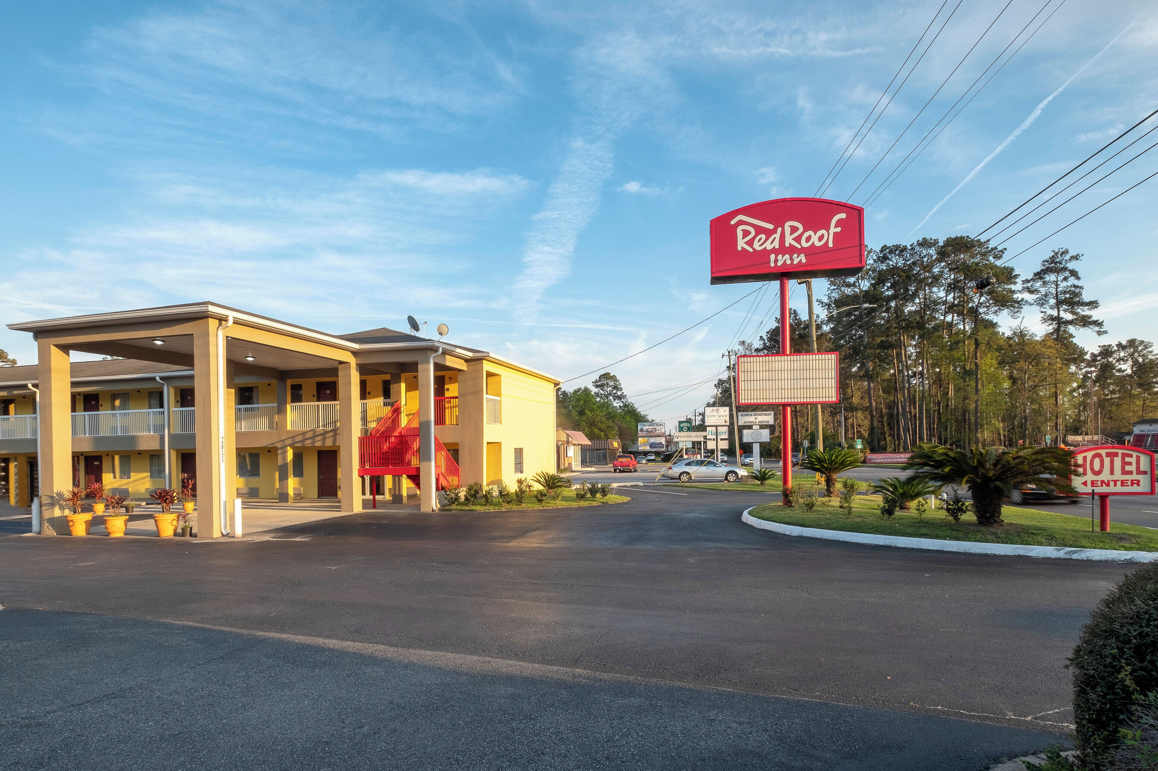 Un motel con un letrero rojo, un área de estacionamiento techado y una carretera que lo lleva a él.