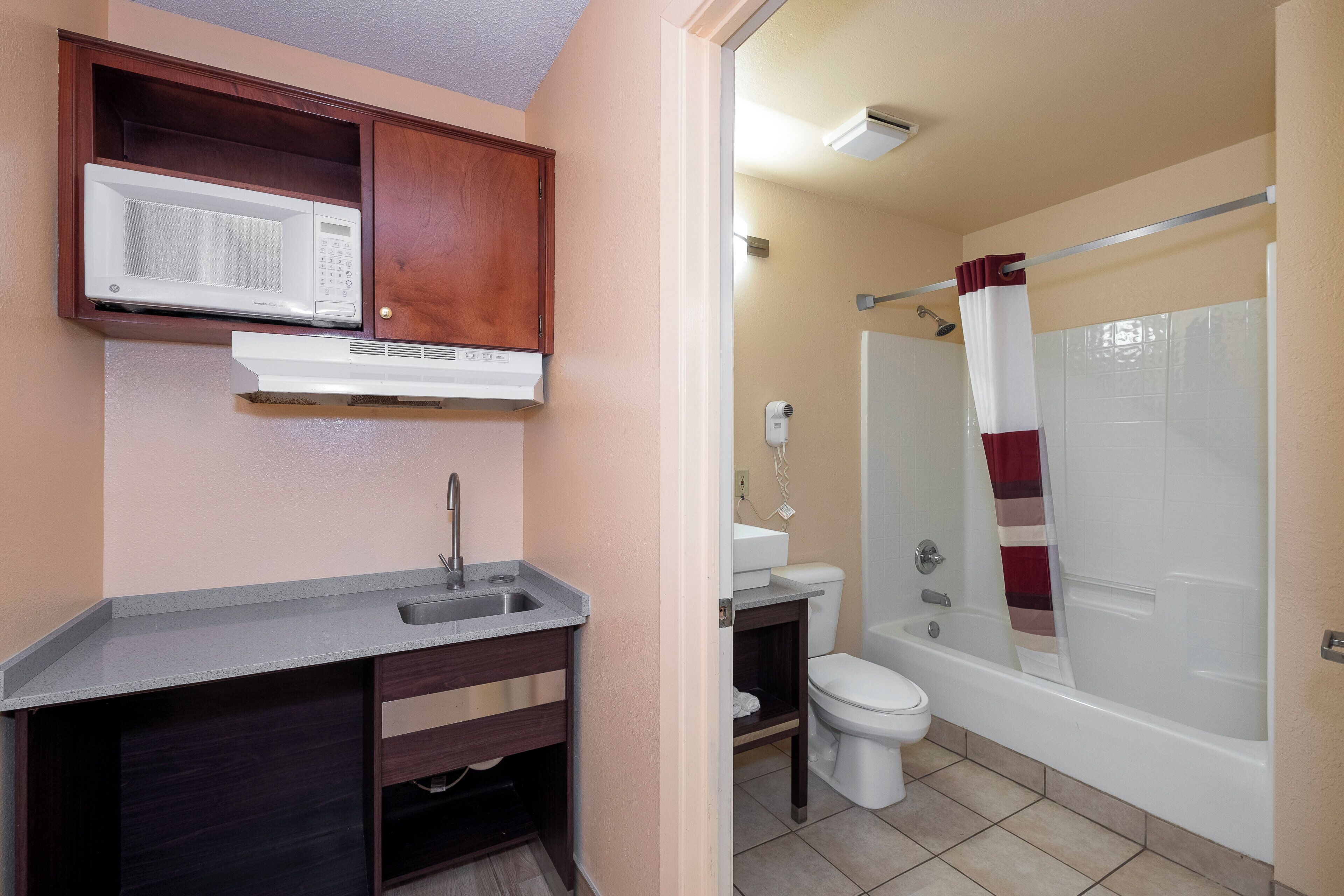 A bathroom with a shower, toilet, sink, and a microwave above the sink.