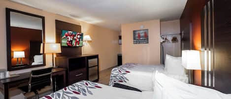 A hotel room with two beds, a desk, a television, and a refrigerator.