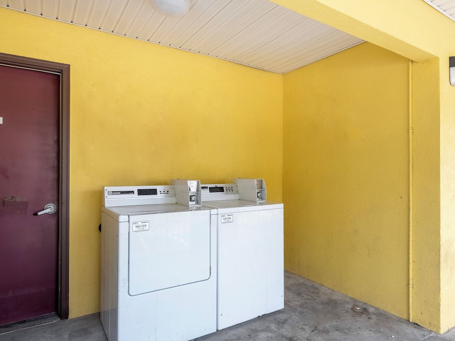 Un área de lavandería con dos lavadoras blancas, una puerta roja y una pared amarilla.
