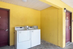 A laundry area with two white washing machines, a red door, and a yellow wall.