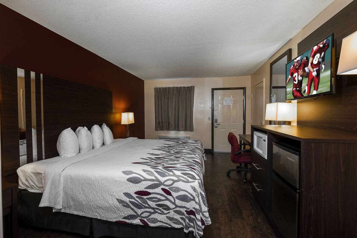 A hotel room with a large bed, a desk with a computer, a television, and a minibar.