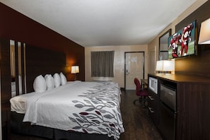 A hotel room with a large bed, a desk with a computer, a television, and a minibar. - Red Roof Inn Valdosta - University (Valdosta)