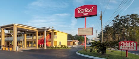Um Red Roof Inn com um prédio de dois andares, área de estacionamento coberta e céu claro.