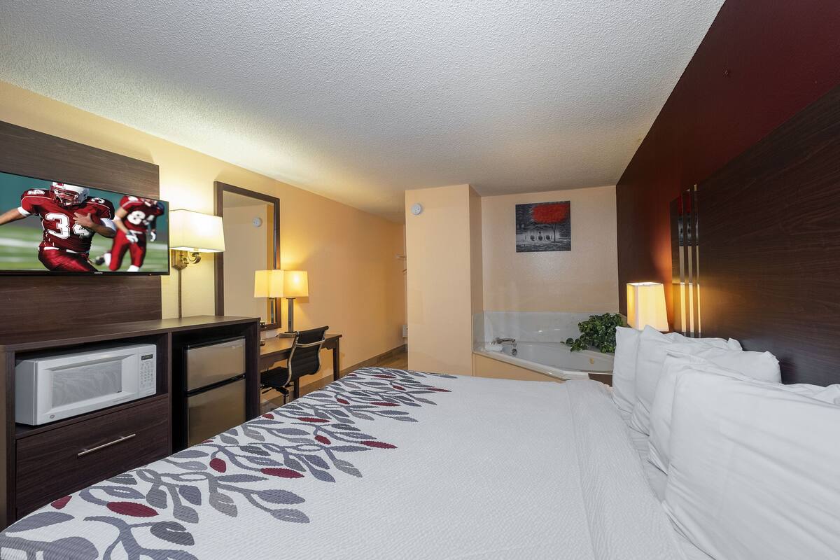 A hotel room with a bed, a TV, a desk, a lamp, and a bathroom.