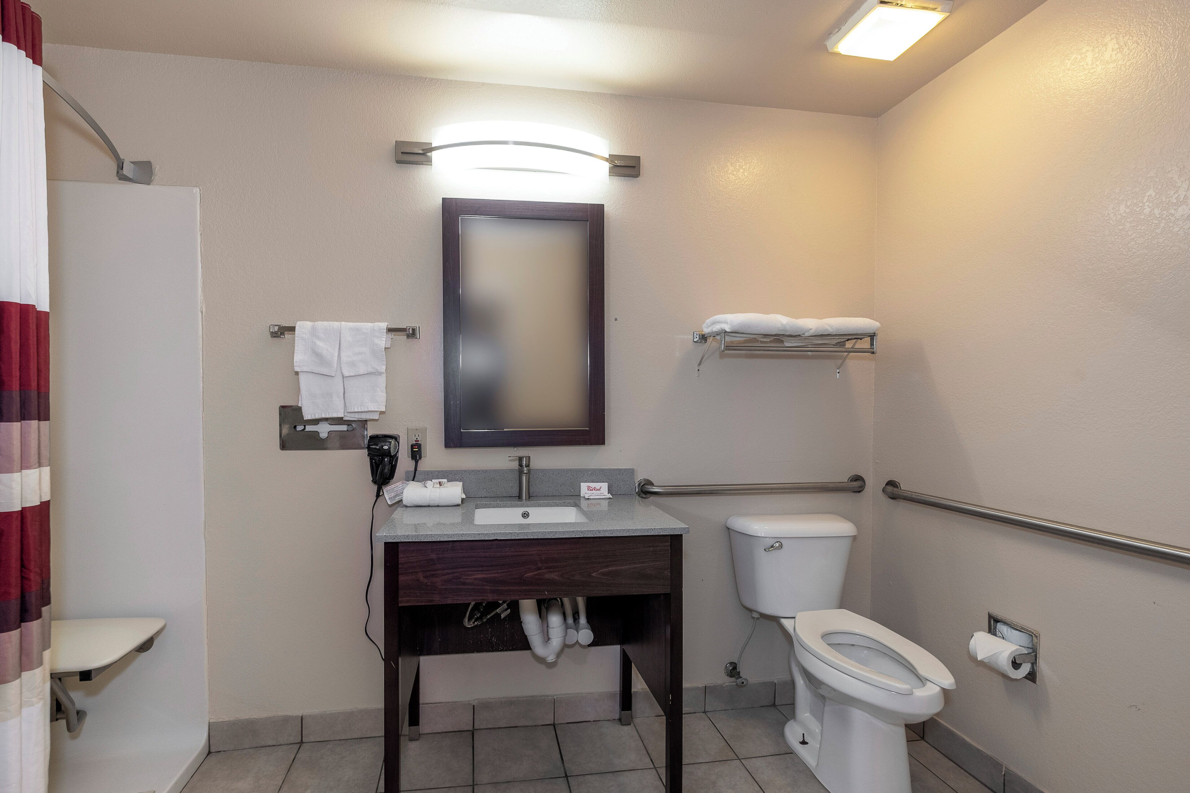 Une salle de bain d’hôtel standard, équipée d’un lavabo, d’un miroir, de toilettes et d’un porte-serviettes.