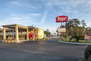 A Red Roof Inn with a yellow building, a covered parking area, and a red sign indicating the hotel entrance. - Red Roof Inn Valdosta - University (Valdosta)