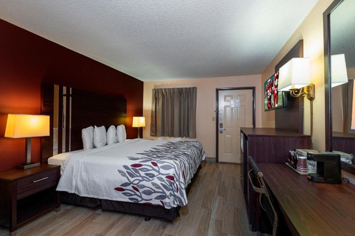 Una habitación de hotel con cama, mesitas de noche, escritorio, espejo y puerta.