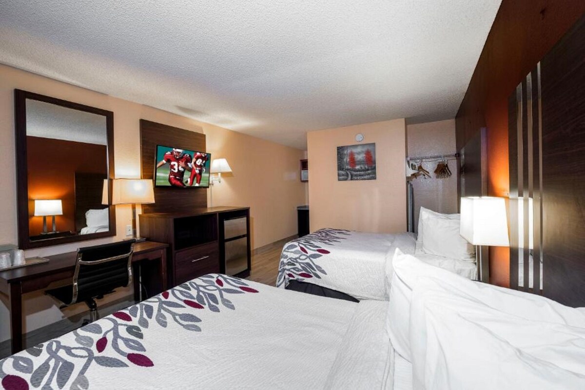 Habitación de hotel con dos camas, un escritorio, un televisor y un espejo.