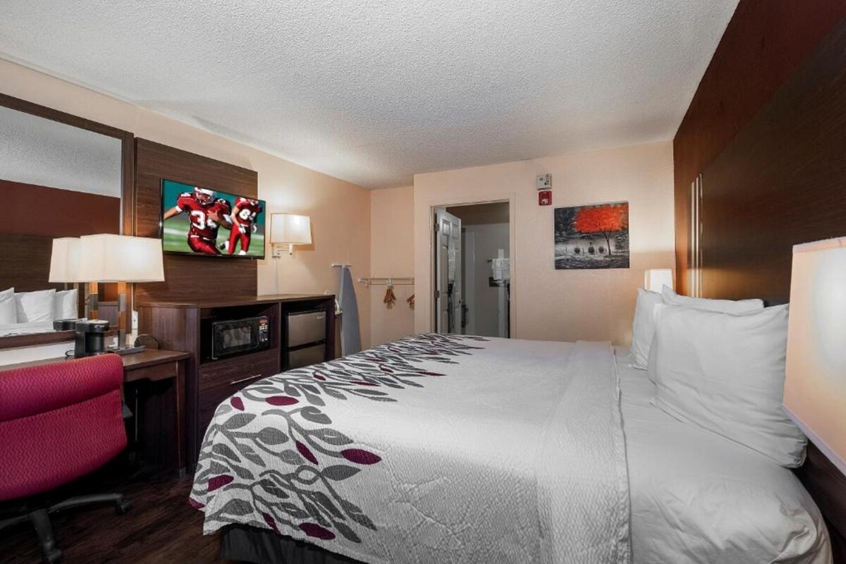 Una habitación de hotel con cama, escritorio, silla, televisor y obras de arte en las paredes.
