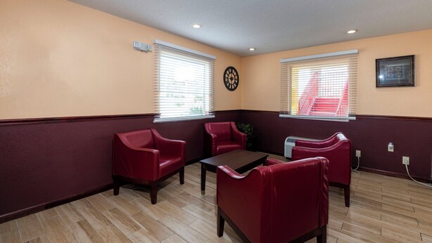 Una habitación con piso de madera, sillones tapizados en rojo, una mesita y dos ventanas con persianas.