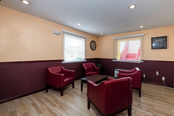 Una habitación con piso de madera, sillones tapizados en rojo, una mesita y dos ventanas con persianas.
