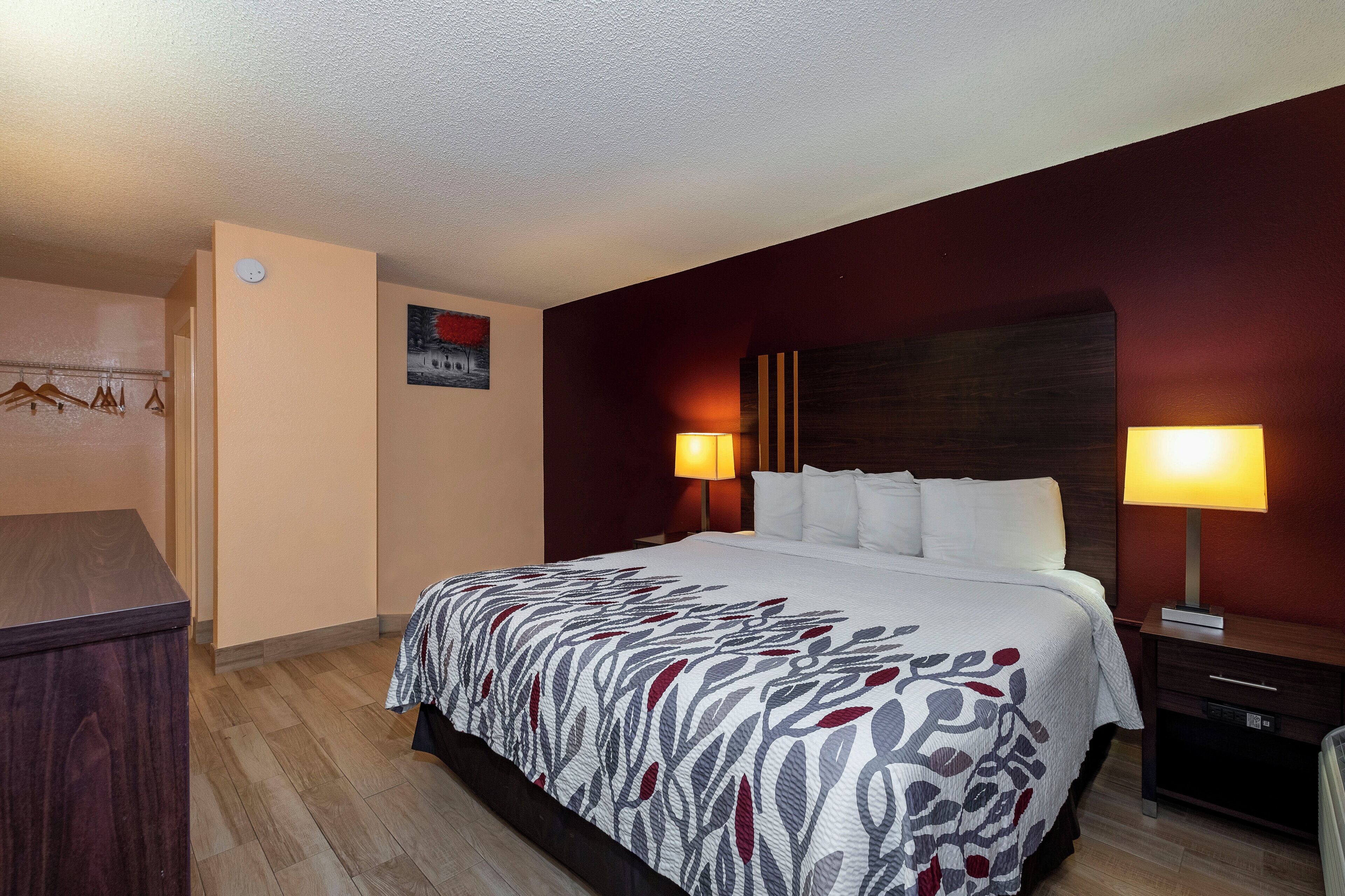 Una habitación de hotel con cama, lámparas de noche, cómoda y un cuadro en la pared.