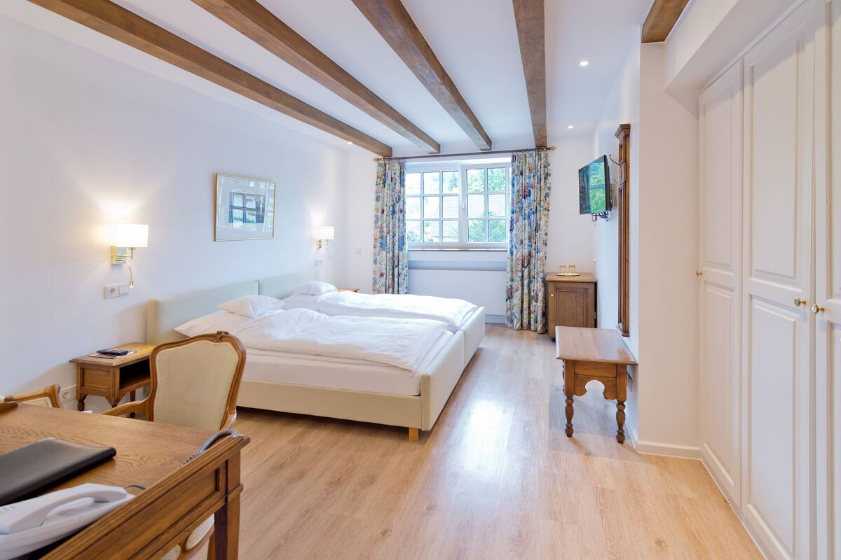 Habitación de hotel con cama, mesita de noche, silla, escritorio y televisor en la pared.