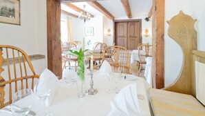 A dining area with wooden chairs and tables, a chandelier, and a wooden door in the background. - Romantik Waldhotel Mangold (Bergisch Gladbach)