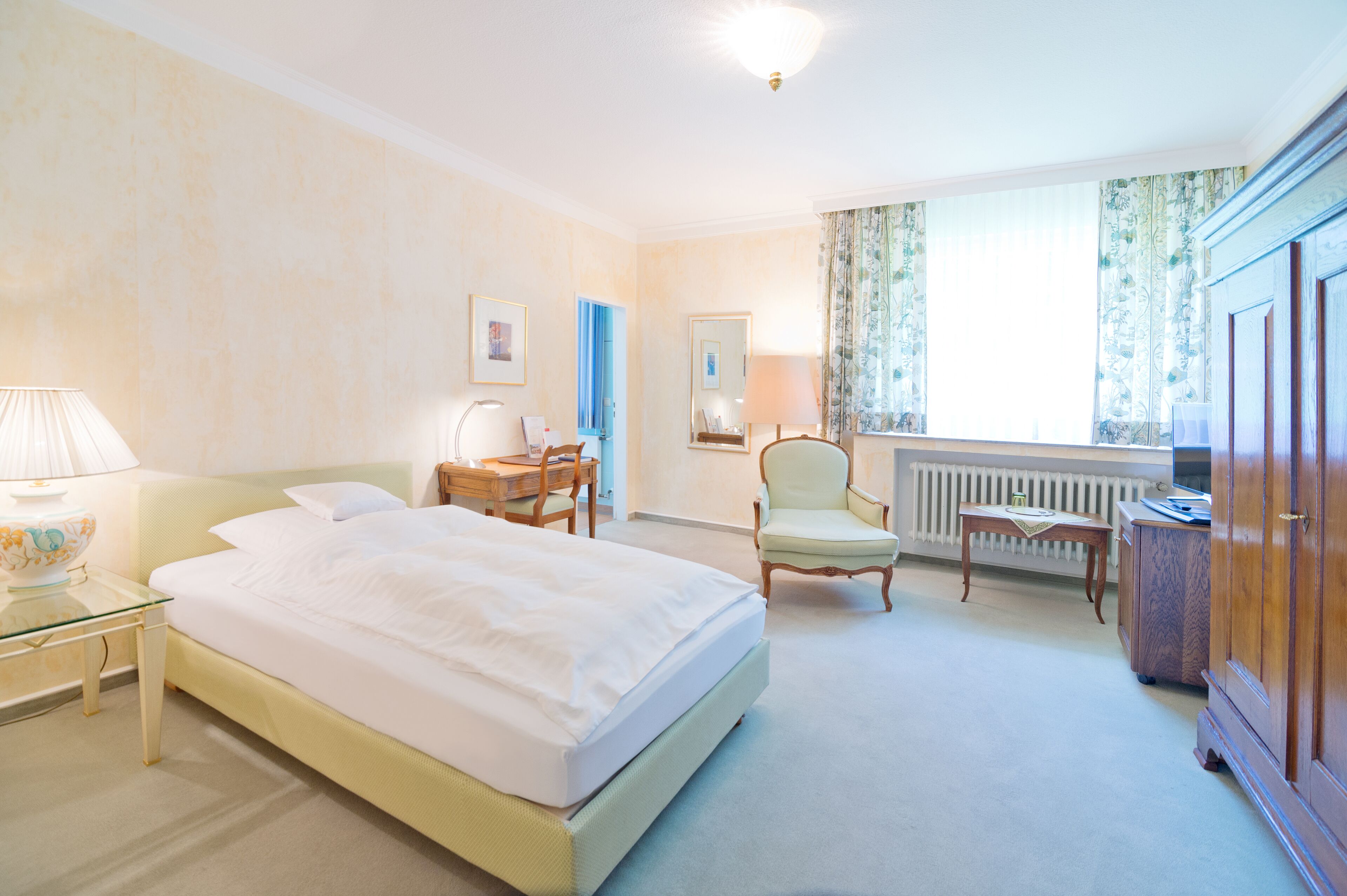 A hotel room with a bed, a desk, a chair, a wardrobe, and a window with curtains.