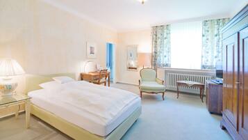 A hotel room with a bed, a desk, a chair, a wardrobe, and a window with curtains.