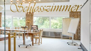 A spacious room with a large window, a whiteboard, and a wooden table. - Romantik Waldhotel Mangold (Bergisch Gladbach)