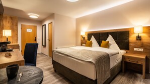 A hotel room with a bed, bedside tables, a desk with a chair, a round table with a cup and spoon, and a door. - AKZENT Hotel Frankenberg (Frankenberg)