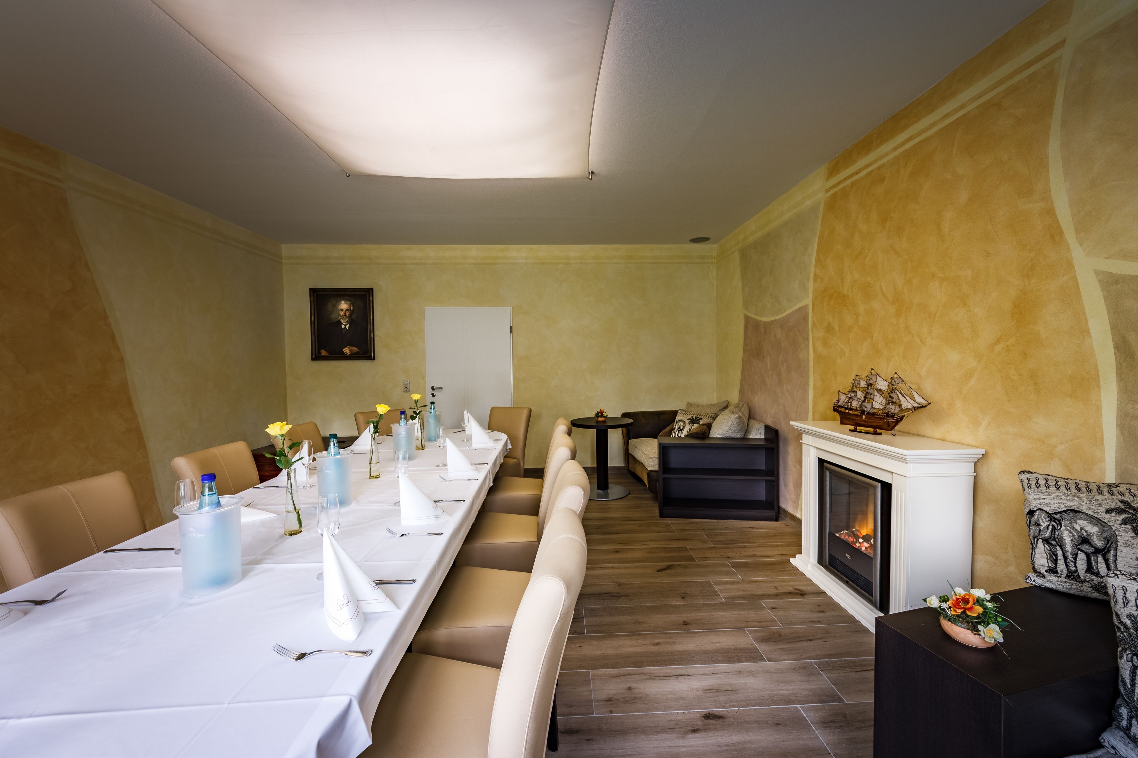 Un coin repas avec une longue table dressée pour le repas, une cheminée et un canapé en arrière-plan.