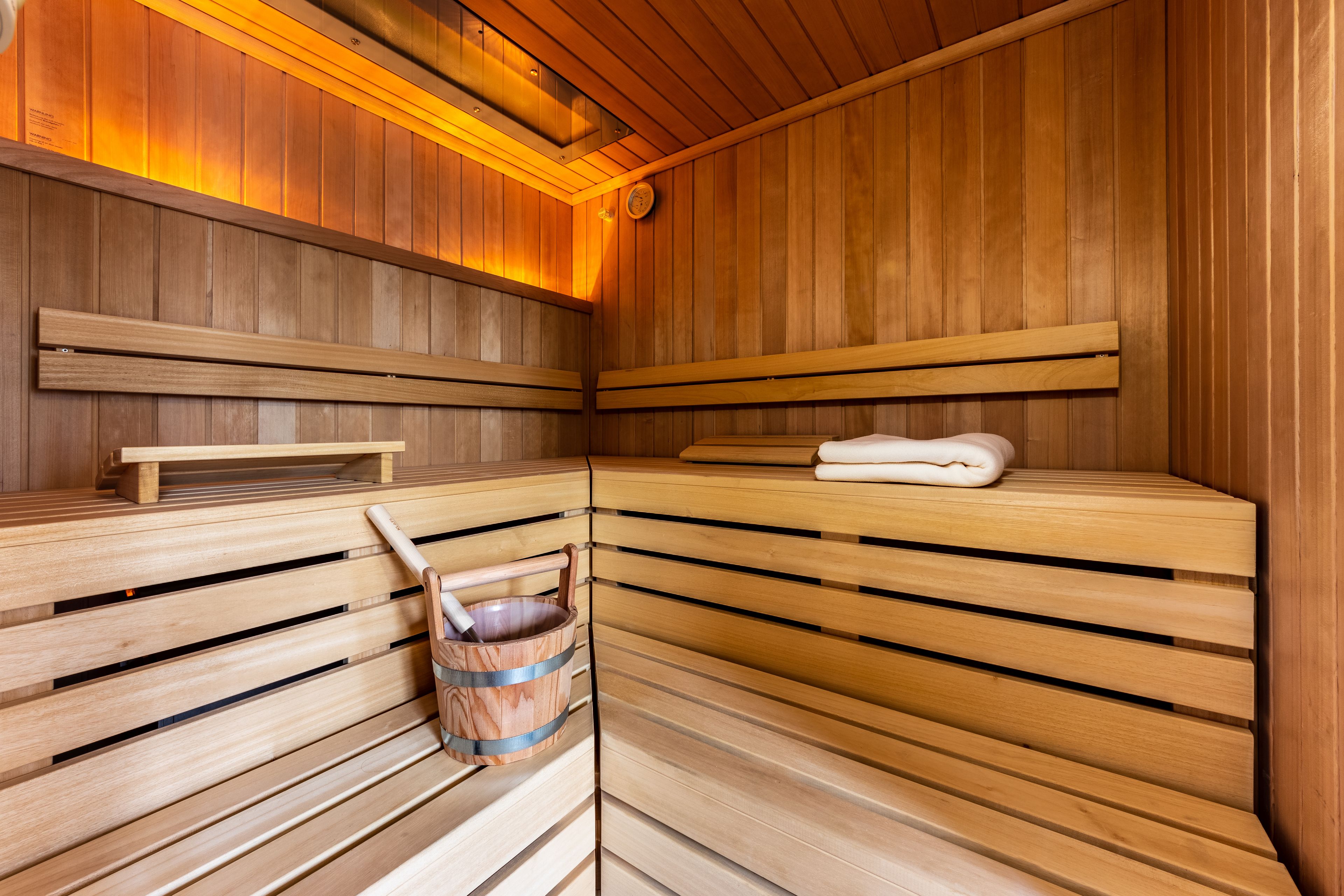 A sauna with wooden benches, a towel, and a wooden bucket.