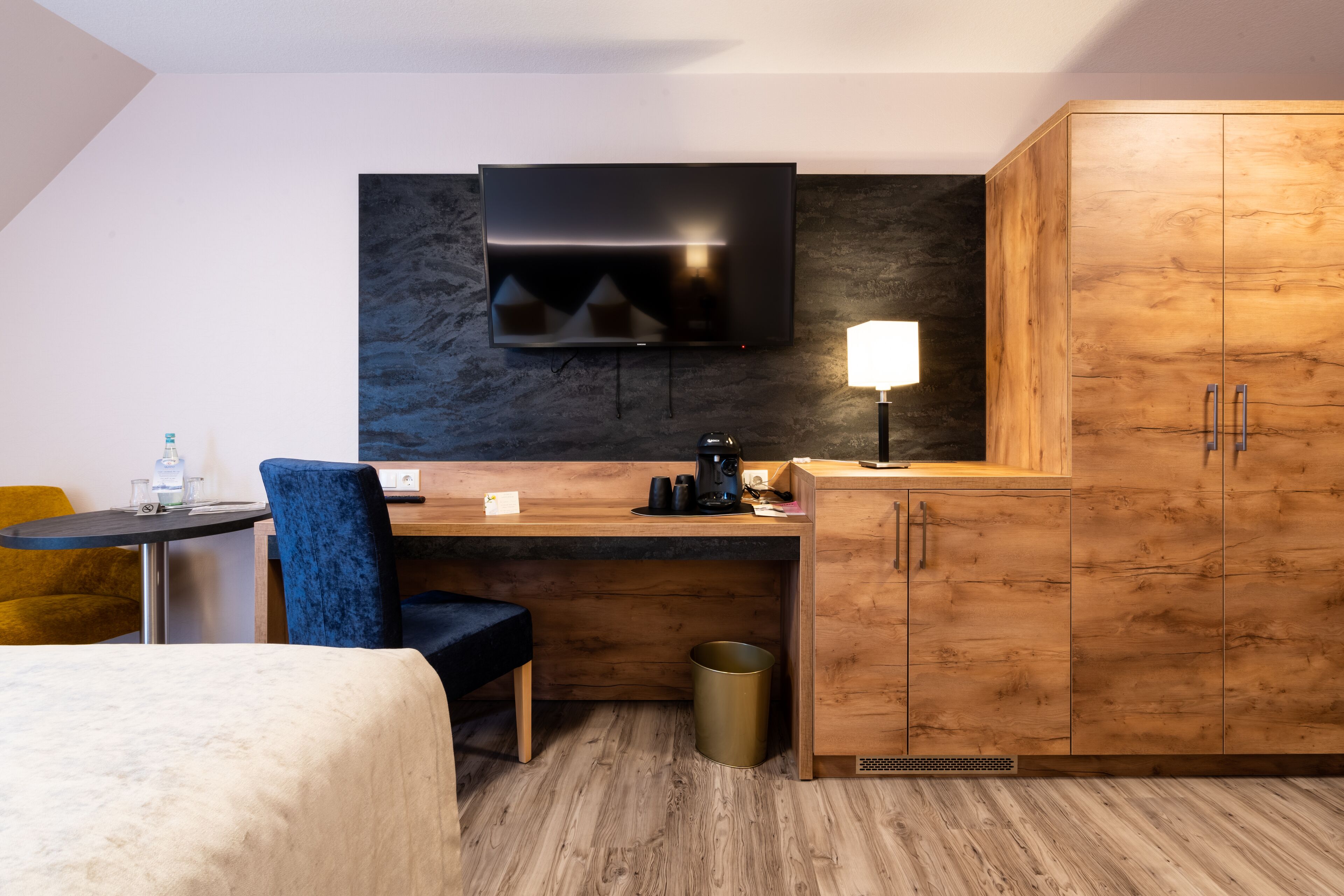 Een moderne hotelkamer met een houten bureau, een flatscreen televisie, een lamp, een stoel, een bed en een prullenbak.
