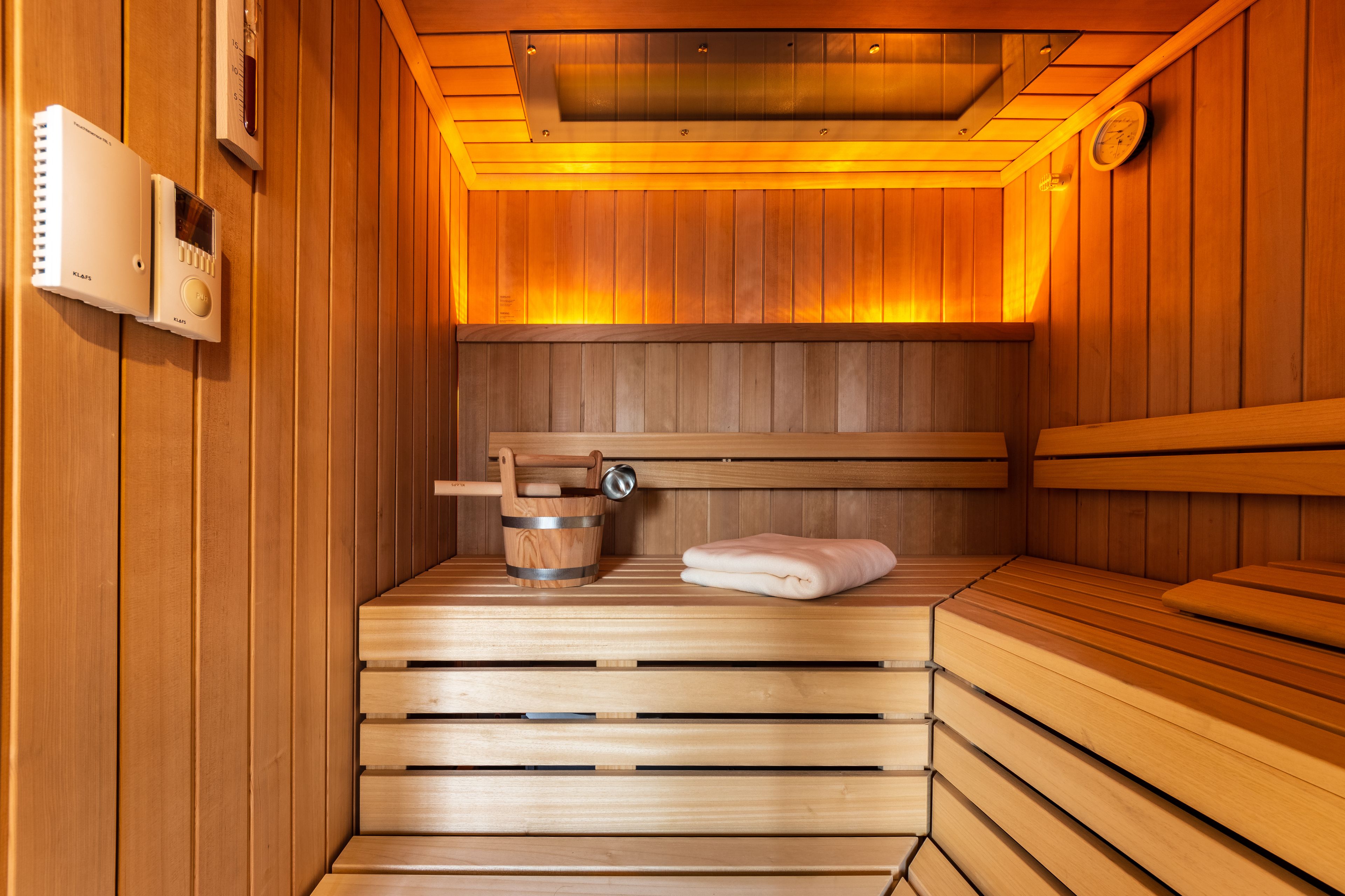 Una sauna con bancos de madera, un cubo de madera y una toalla.