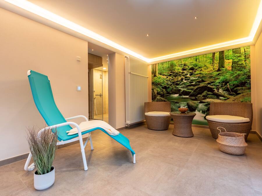Un espace spa moderne doté d’un fauteuil de relaxation, de meubles en osier et d’une fresque murale sur le thème de la forêt.